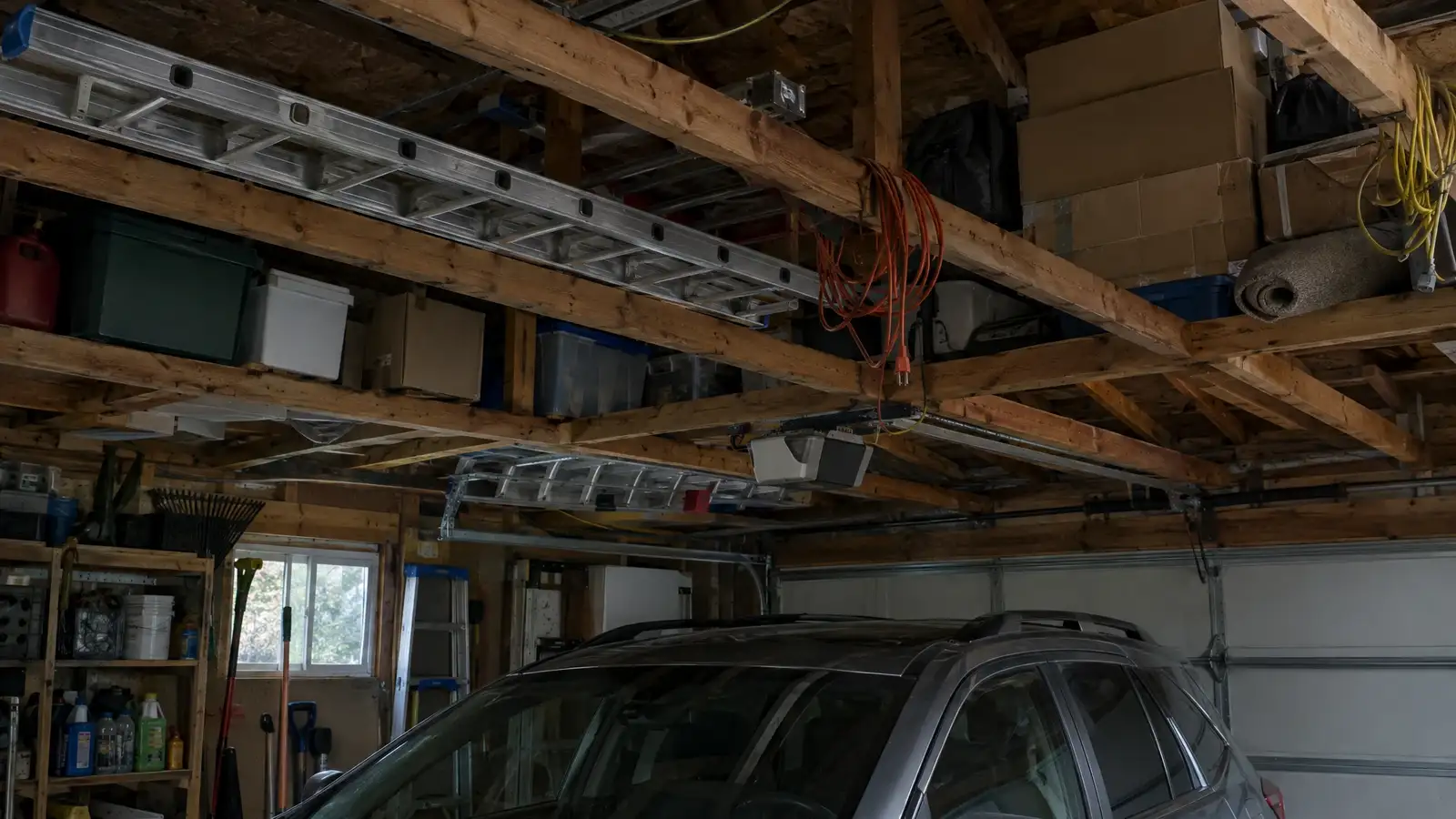Before: a garage ceiling stacked with boxes, ladders and draped cords above a car